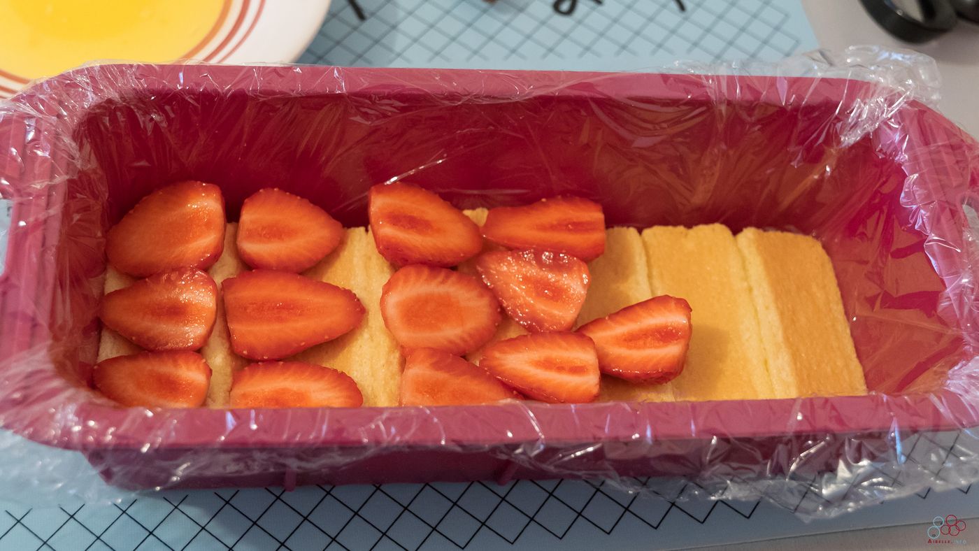 Photo of the mold containing a layer of biscuits underneath and a layer of sliced ​​strawberries on top.